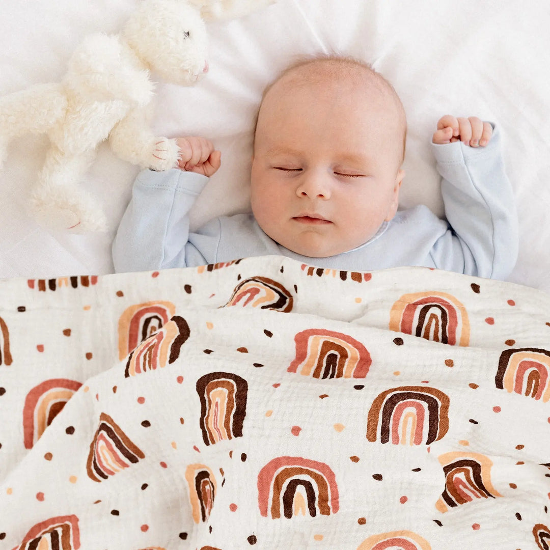 A peaceful baby sleeping under a cozy blanket with rainbow designs, accompanied by a soft bunny plush toy.