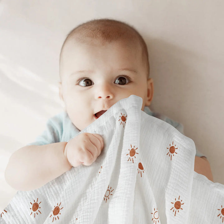 Adorable baby holding an ultra-soft Minky baby blanket featuring a cheerful sun print design - ideal for cuddling and comfort.