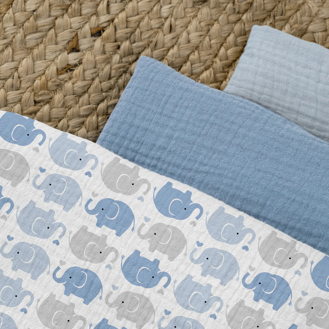 Close-up detail of muslin swaddle blanket set featuring blue and grey elephant pattern print with textured cotton fabric shown on natural jute rug background