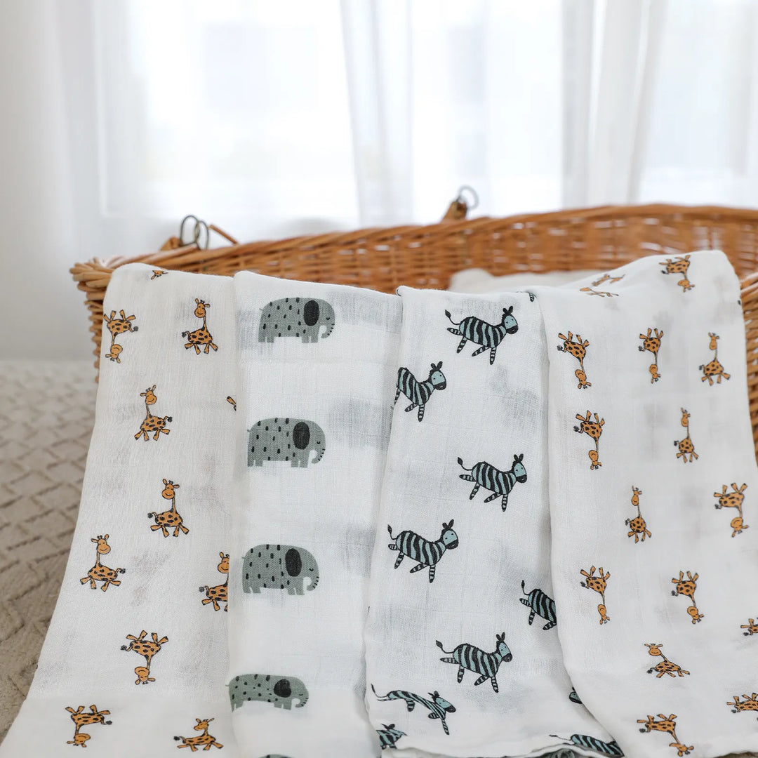 Three muslin swaddle blankets with animal prints featuring giraffes, hippos, and zebras, draped over a wicker basket. Soft and gentle for babies.