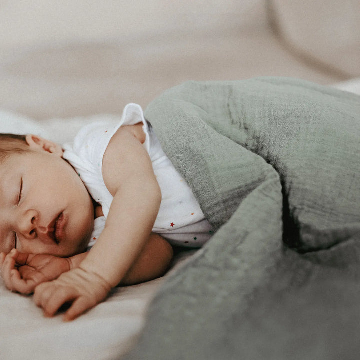 Baby sleeping wrapped in a soft, breathable, green Organic Cotton Muslin Swaddle Blanket, offering comfort and gentle warmth.