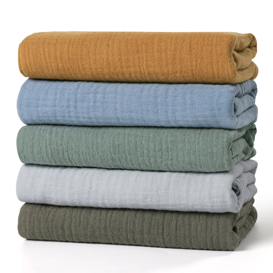 Stack of 5 Organic Cotton Muslin Swaddle Blankets in Mustard, Blue, Sage, Grey, and Olive, showcasing soft and breathable texture for babies.