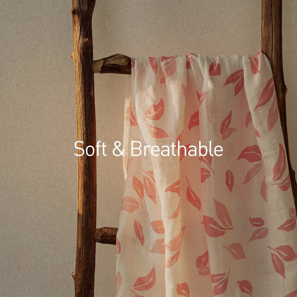 Close-up of a pink leaf-patterned muslin swaddle blanket draped on a rustic wooden ladder, labeled 'Soft & Breathable.' Ideal for newborns and infants.